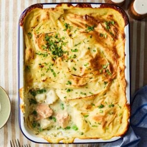 A bird's eye view of a Fish Pie, with a portion missing after being served. Showing the filling of chunky fish, peas and a creamy white sauce.