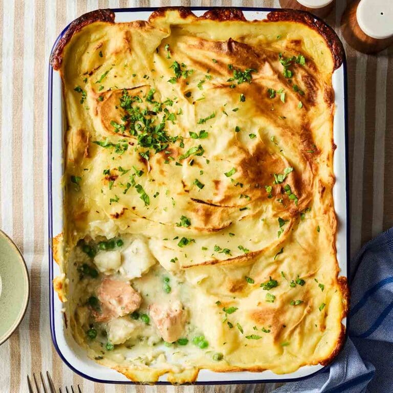 A bird's eye view of a Fish Pie, with a portion missing after being served. Showing the filling of chunky fish, peas and a creamy white sauce.