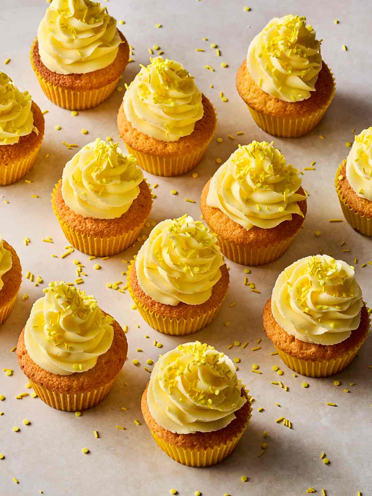 Rows of finished Lemon Cupcakes with yellow buttercream and sprinkles on top.