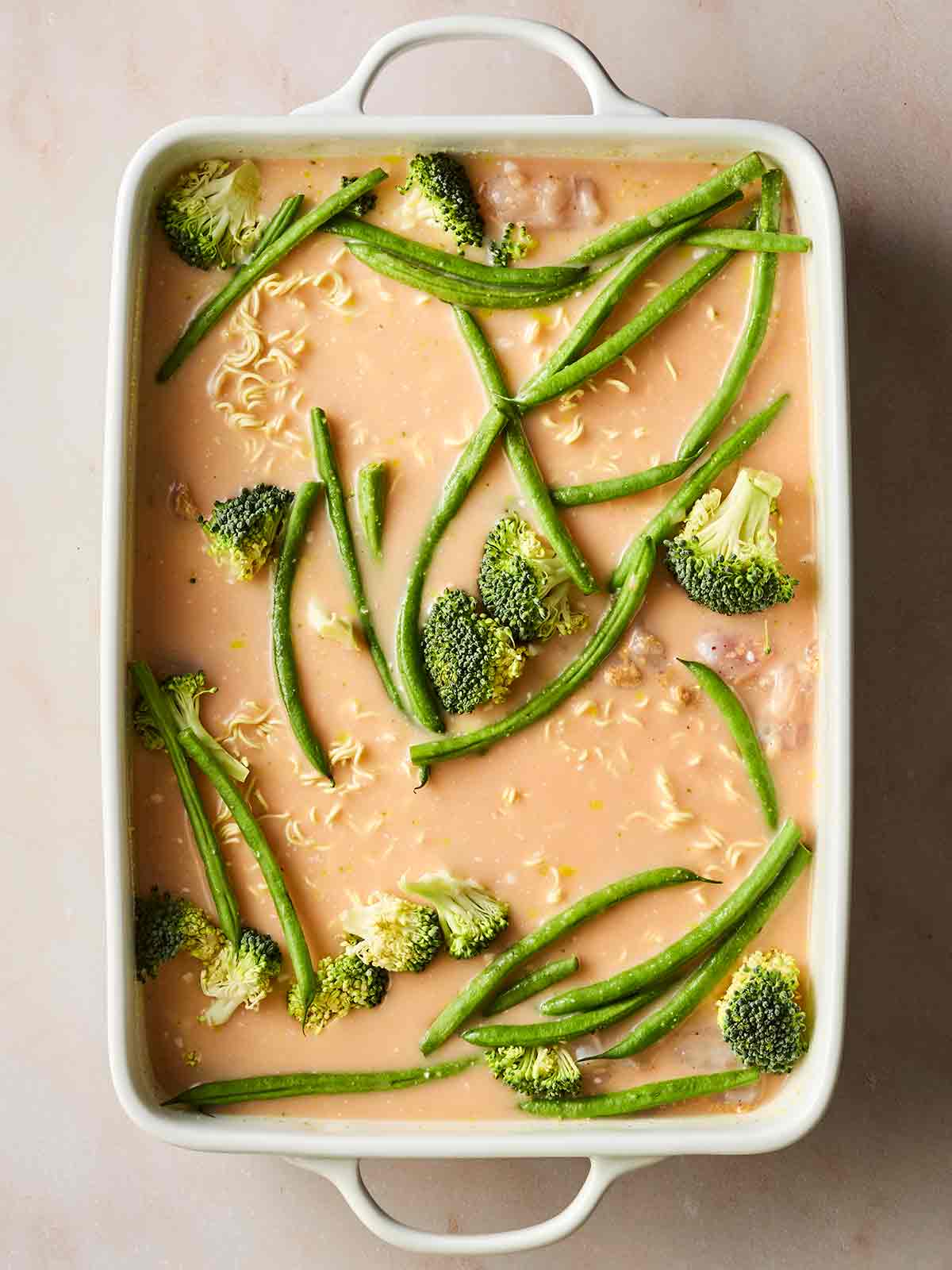 An oven dish with coconut milk liquid, noodles and chicken underneath, vegetables on top, ready to go in the oven.