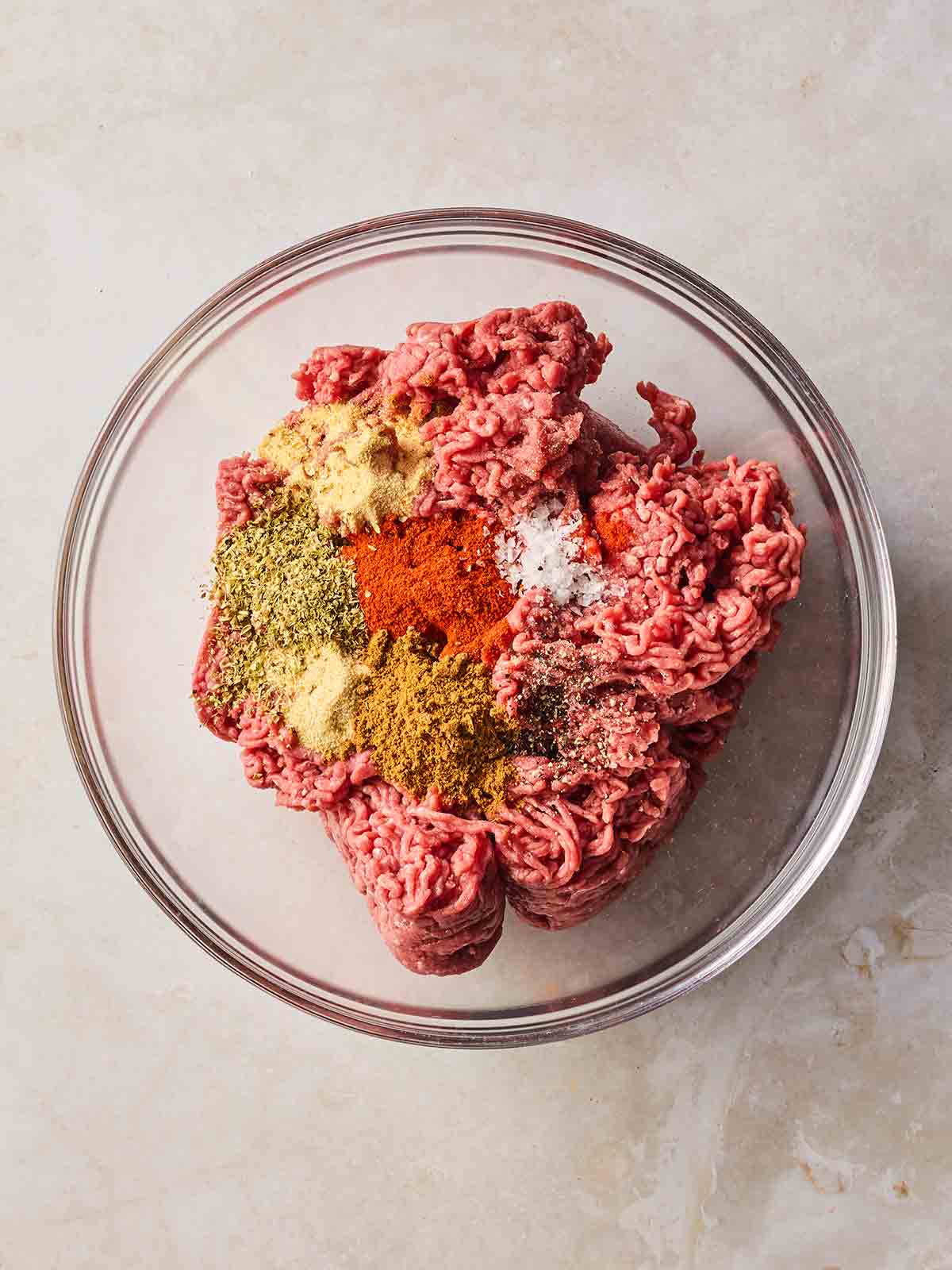 A glass bowl with beef mince inside, with lots of herbs and spices.