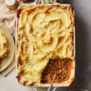 A vegetarian cottage pie straight out of the oven with a golden brown top and a portion already dished out with a spoon.