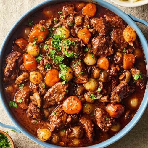 A pot of Beef Bourguignon, on a table with mashed potatoes to the side.