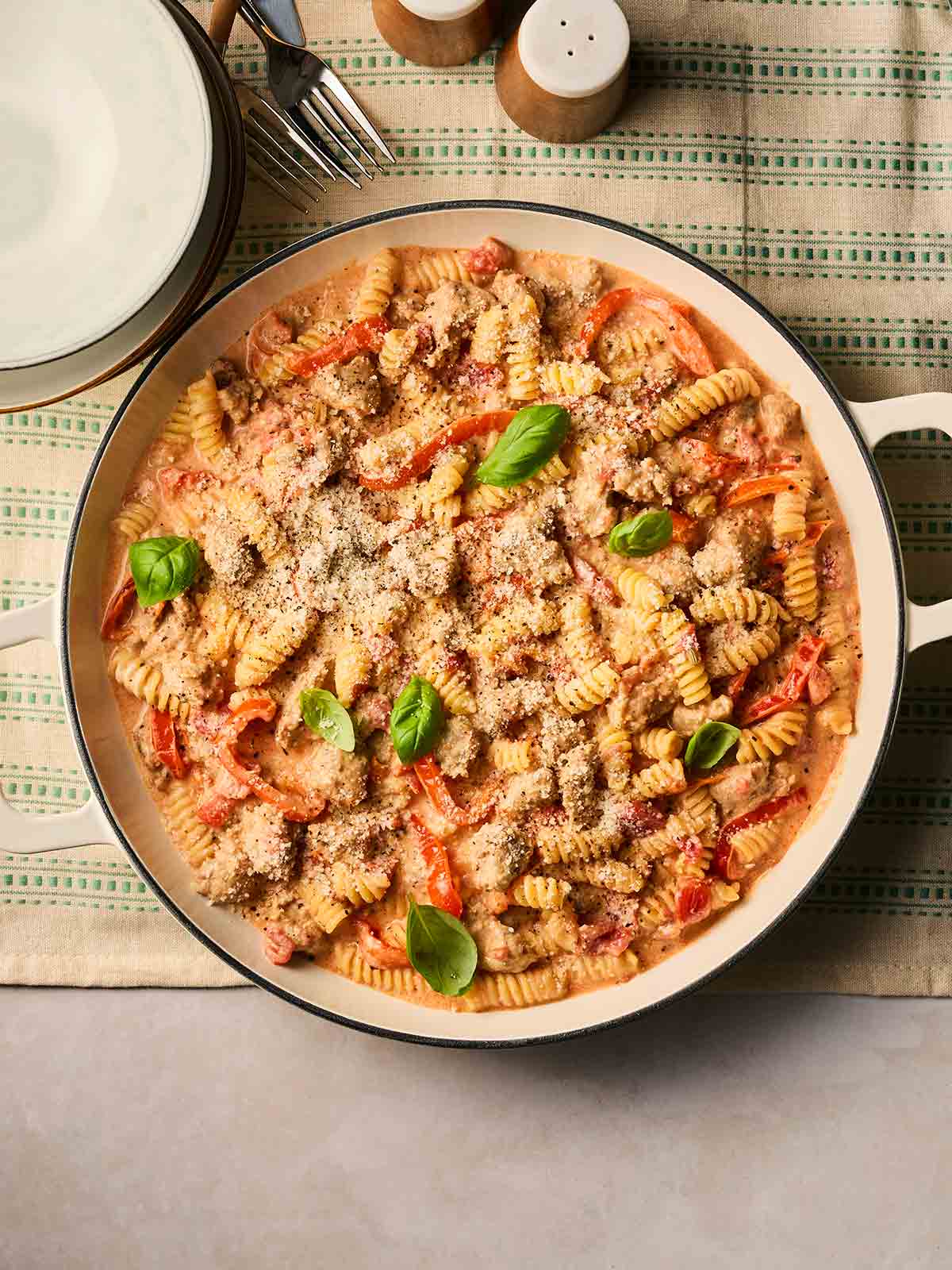 A pan filled with a one pot pasta of Sausage and tomato sauce, topped with fennel, on a tablecloth, ready to serve.