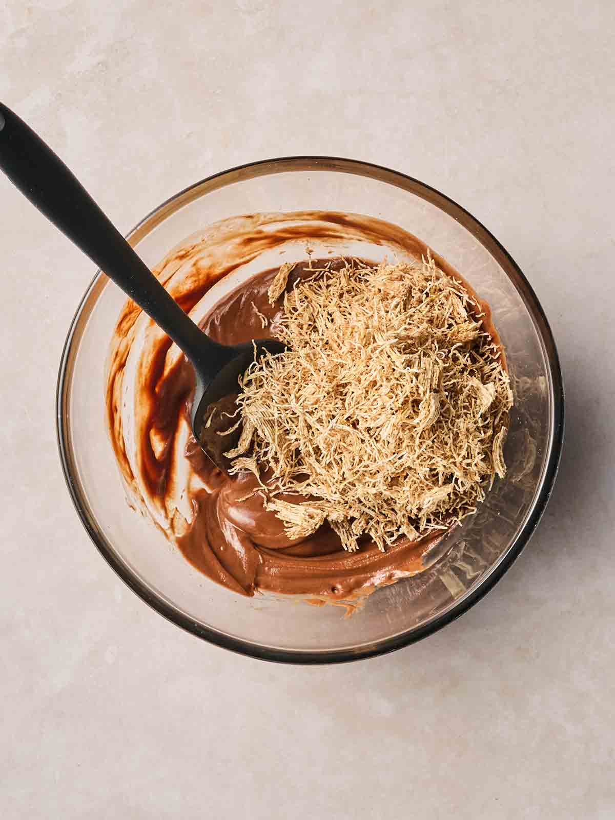 Broken up shredded wheat in a bowl with melted chocolate, being mixed together with a spoon.