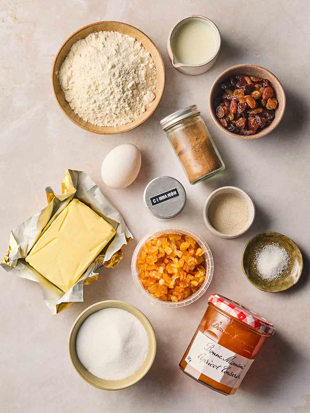The ingredients for making Hot Cross Buns lay out in bowls on a white counter.