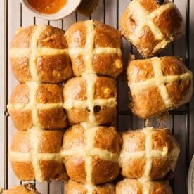 Rows of just-baked Hot Cross Buns on a wire rack, ready for the apricot jam glaze.