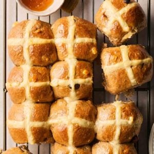 Rows of just-baked Hot Cross Buns on a wire rack, ready for the apricot jam glaze.