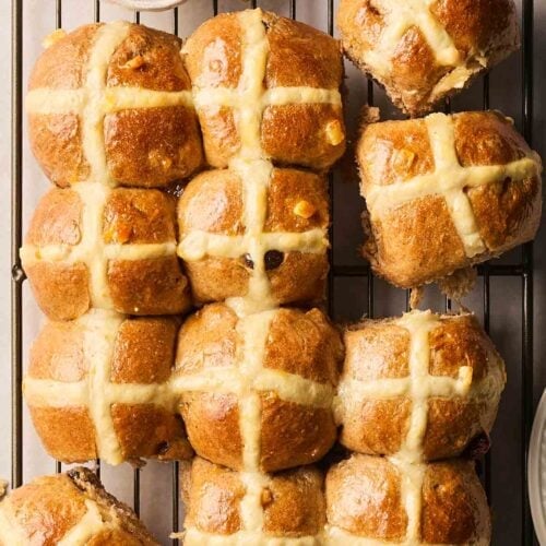 Easter buns, AKA Hot Cross Buns, ready to serve from a wire rack, with a small bowl of apricot jam to the side, with a brush to brush it on.