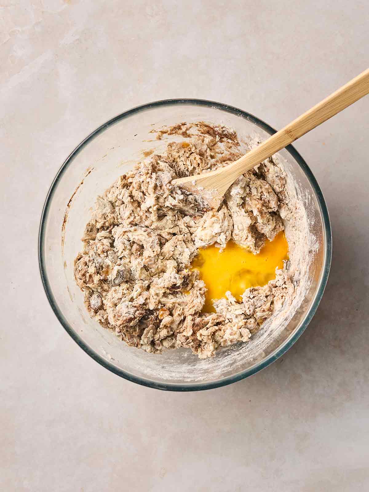 A glass bowl with a dough and spoon, and beaten egg poured in.