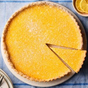 A Lemon Tart with a slice cut out, ready to serve, on a table.