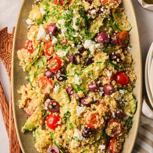 A quinoa salad on a platter with cucumber, tomatoes, olives and feta, ready to be served.