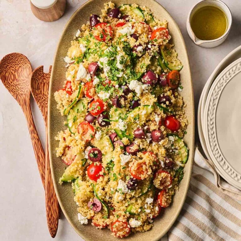 A plate on the dining table with quinoa, tomatoes, cucumbers, olives and feta.