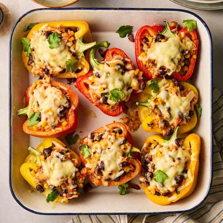 A close up of a pepper cut in half in a roasting dish, filled with rice and vegetables, with melted cheese on top.