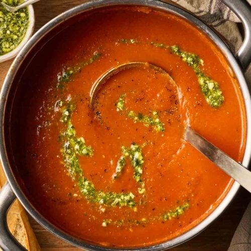 A pan of tomato soup with pesto, ready to dish up with a ladle.