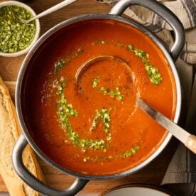 A close up of a big pan of tomato soup with green pesto on top, ready to serve into bowls.