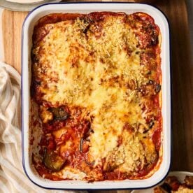 A baked Aubergine Parmigiana with a portion missing on a table, ready to serve the rest.
