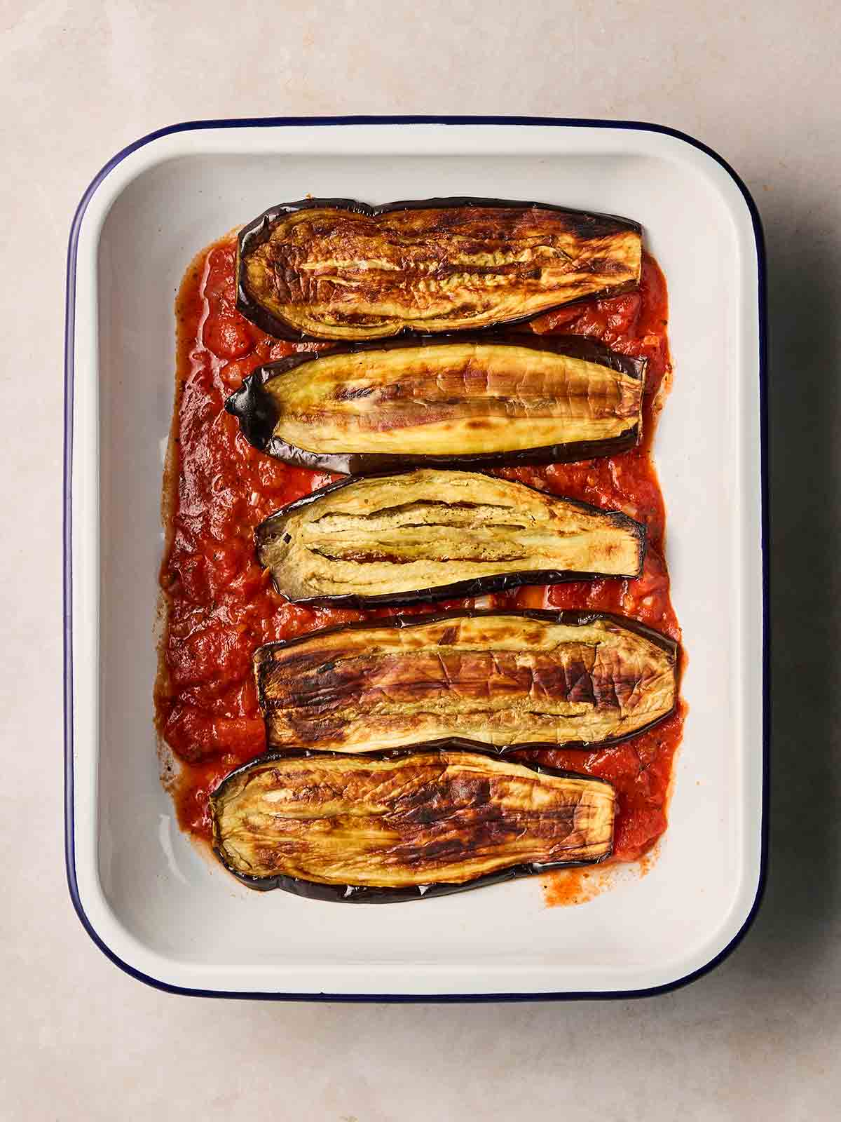 A white oven dish with tomato sauce in the base, with sliced aubergine on top, to start layering.