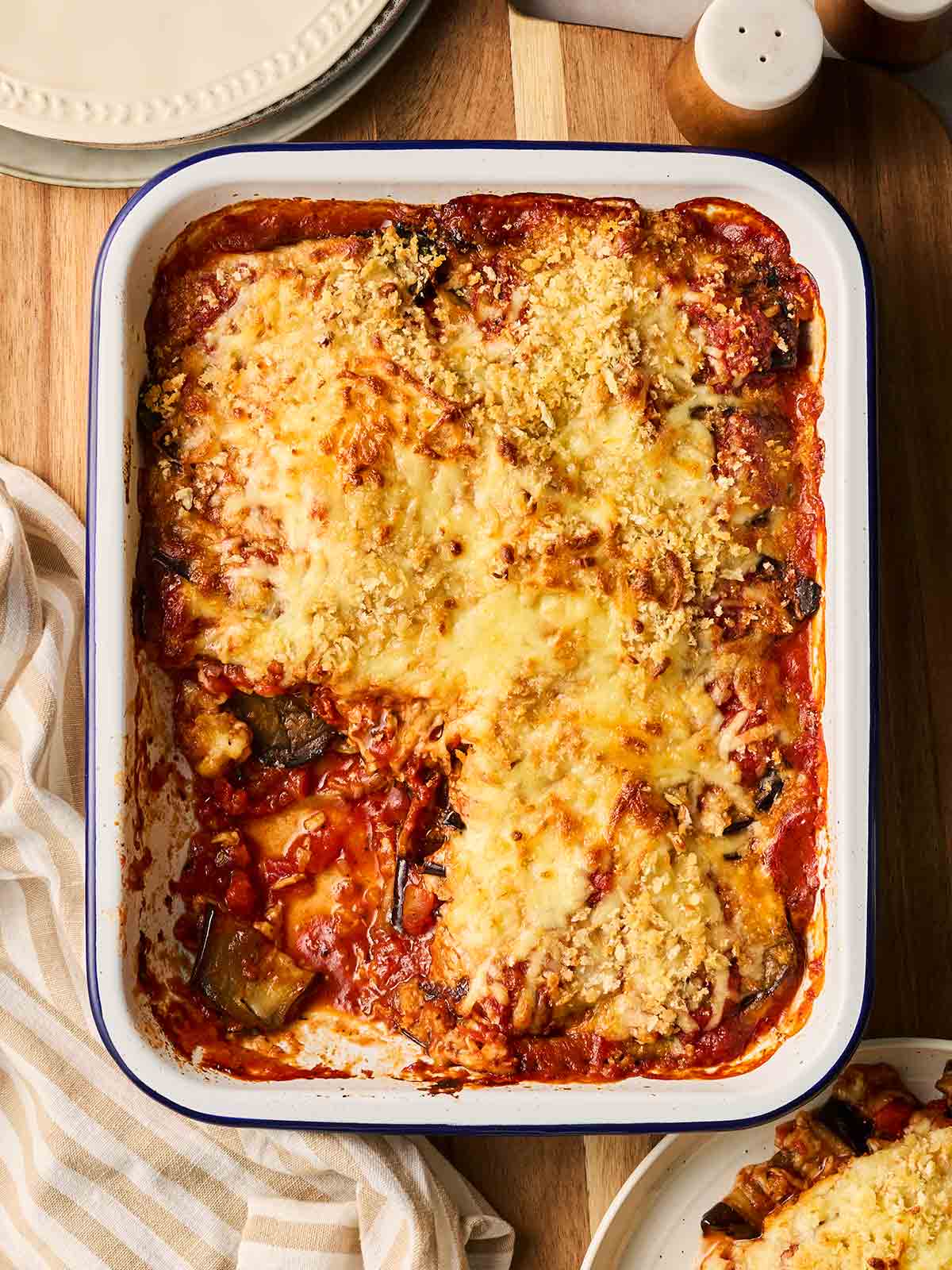 A baked Aubergine Parmigiana on a table, with one portion missing, showing the layers of vegetables, cheese and sauce.