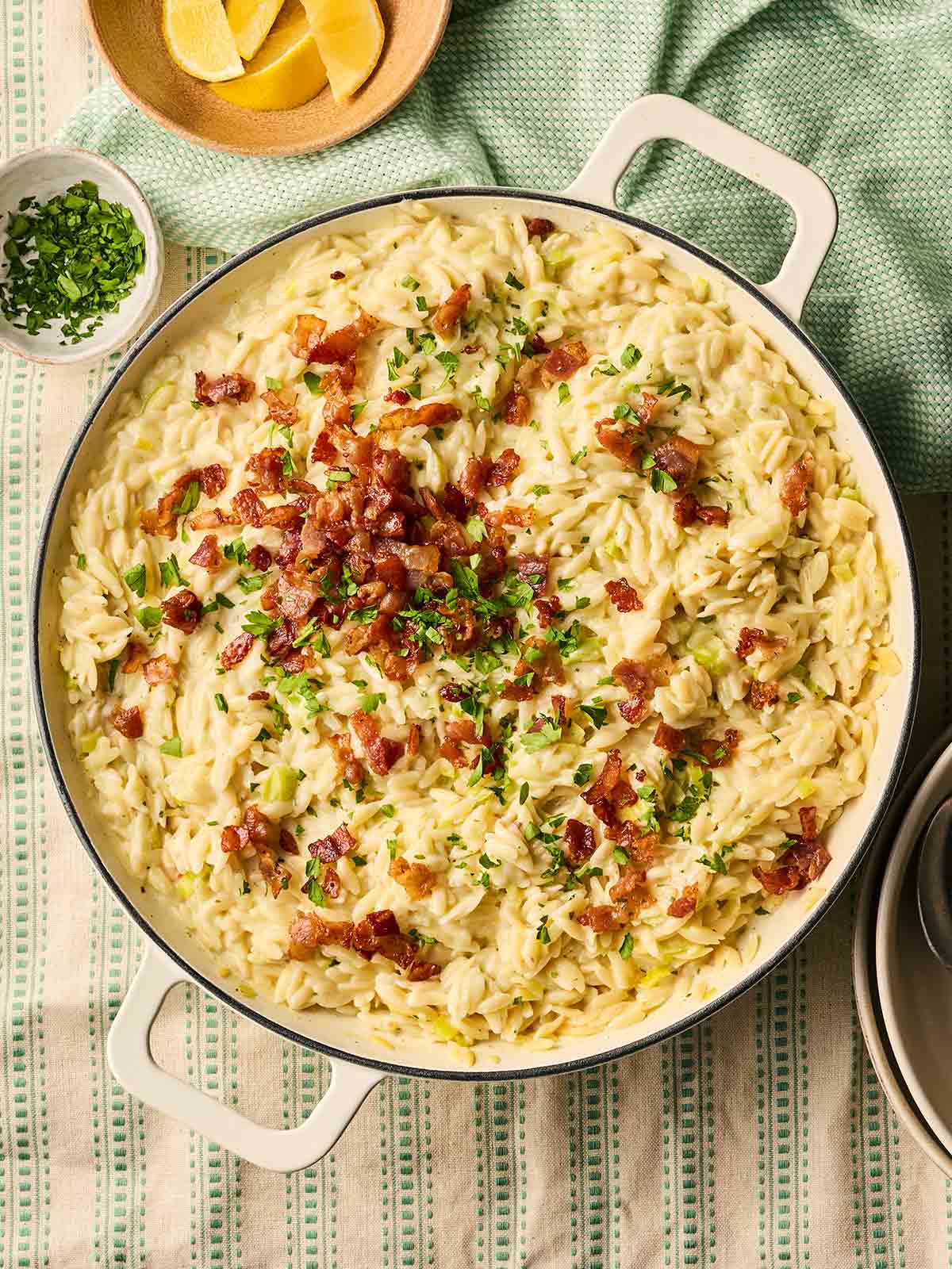 A pan filled with with Bacon and Leek Orzo with bacon bits and parsley over the top, on a table, ready to serve.