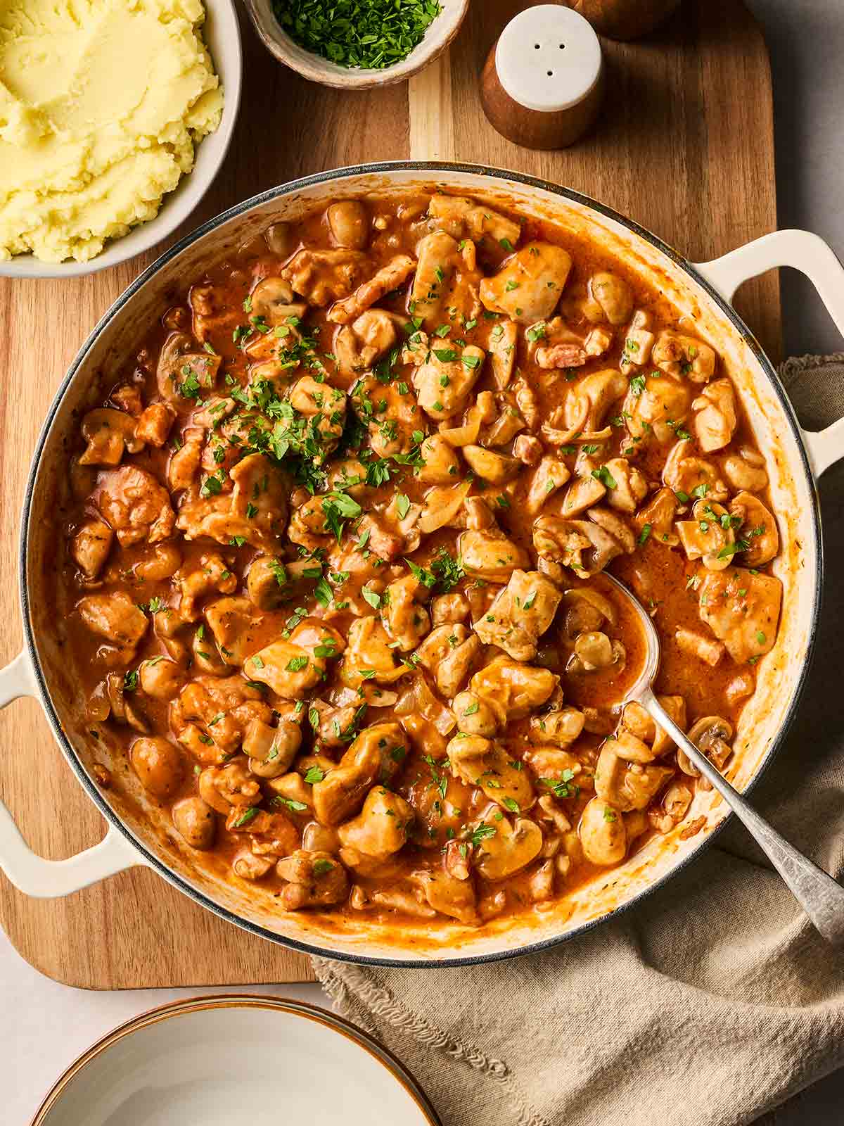 A large pot of chicken chasseur on a table, ready to serve with mashed potatoes and green beans on the side.