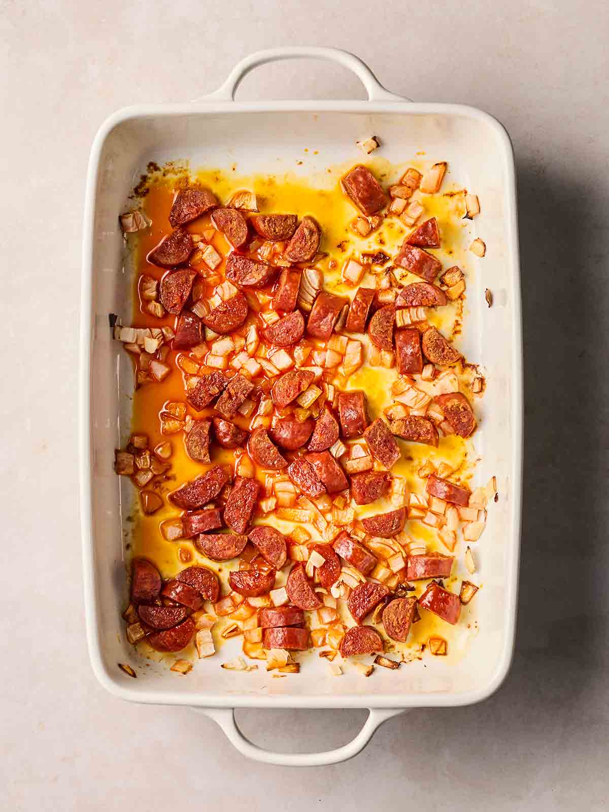 An oven dishwasher with sliced chorizo and onion, having been baked a little so the oils have been released.