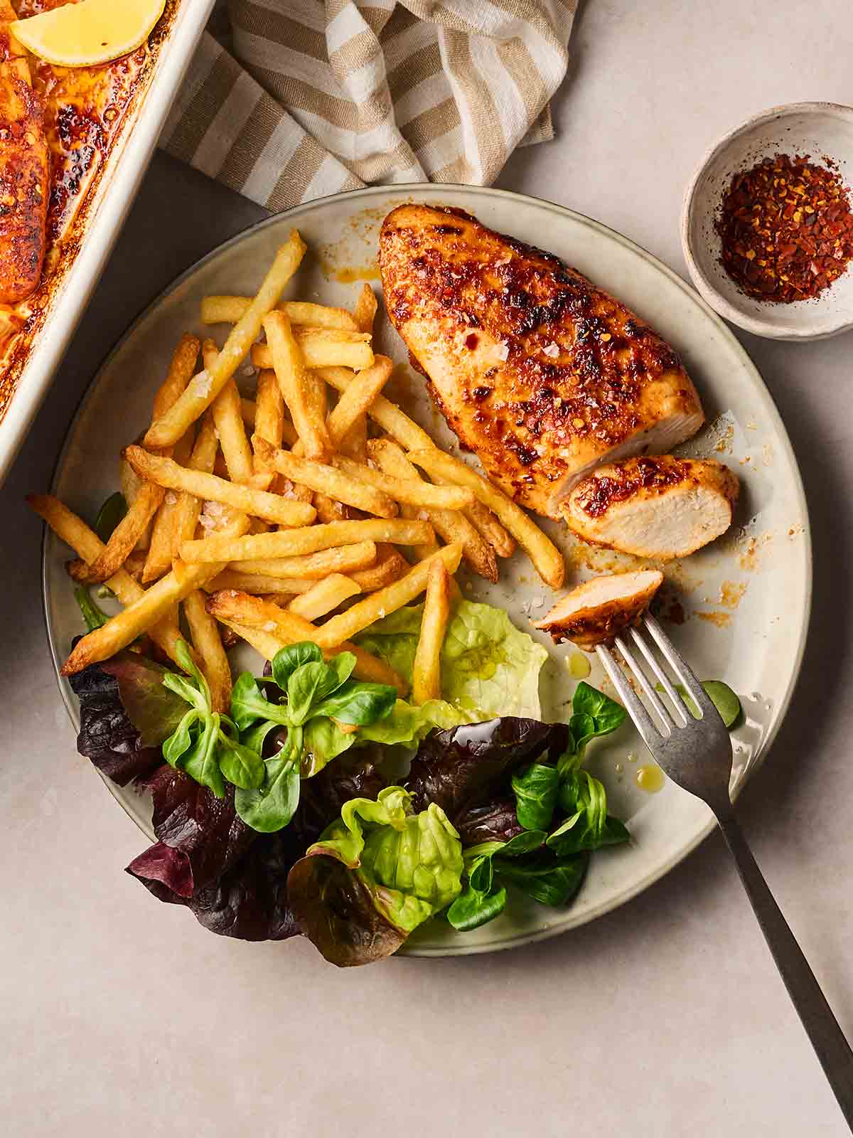 A plate of chicken breast known as Divorce Me Chicken, fries and green salad, with a fork, ready to eat.