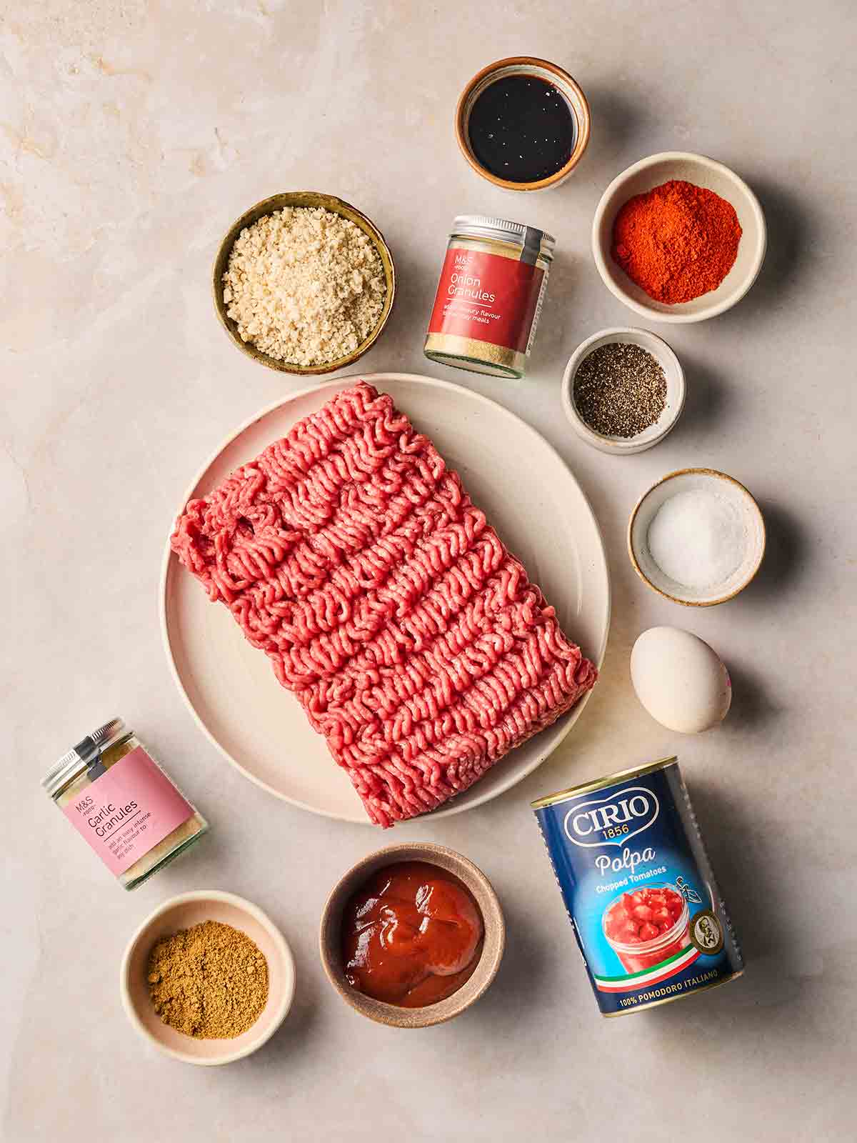 The ingredients to make homemade meatloaf in bowls and plates on a white surface.