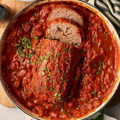 A pan of meatloaf in a pan, ready to serve up, with a bowl of mashed potato to the side.
