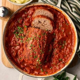 A bowl of tomato sauce with meatloaf in the middle, with a few slices and parsley on top.