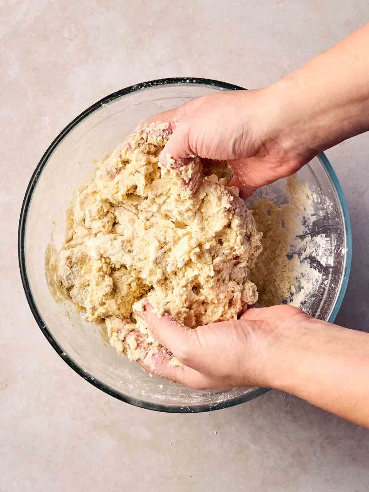 Two hands showing a Cheese Scone dough over a glass bowl.