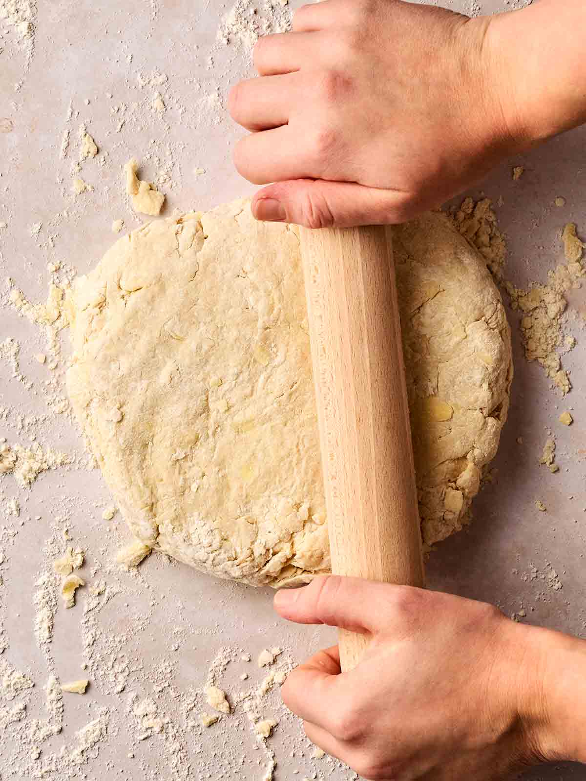 Two hands rolling out a floury mixture with a rolling pin for making Cheese Scones.