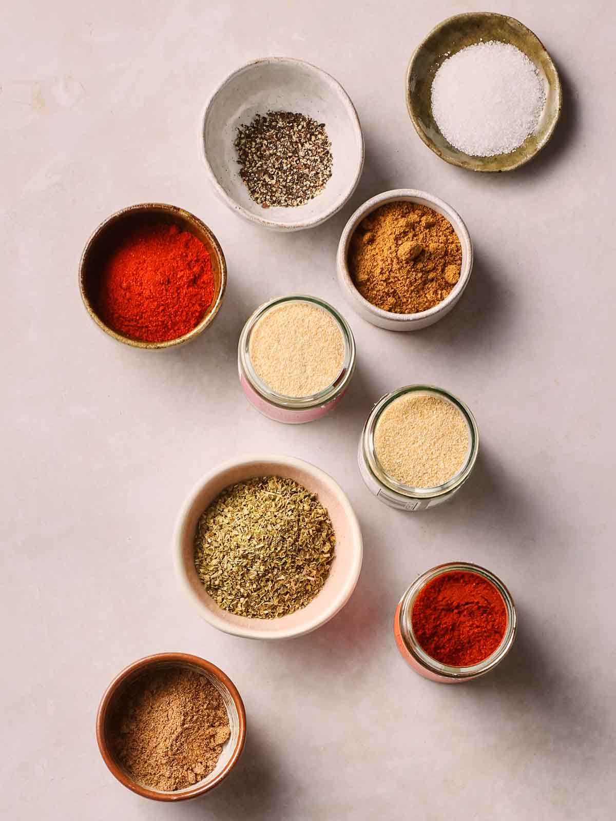 Pots of spices on a white surface that make up Fajita Seasoning.