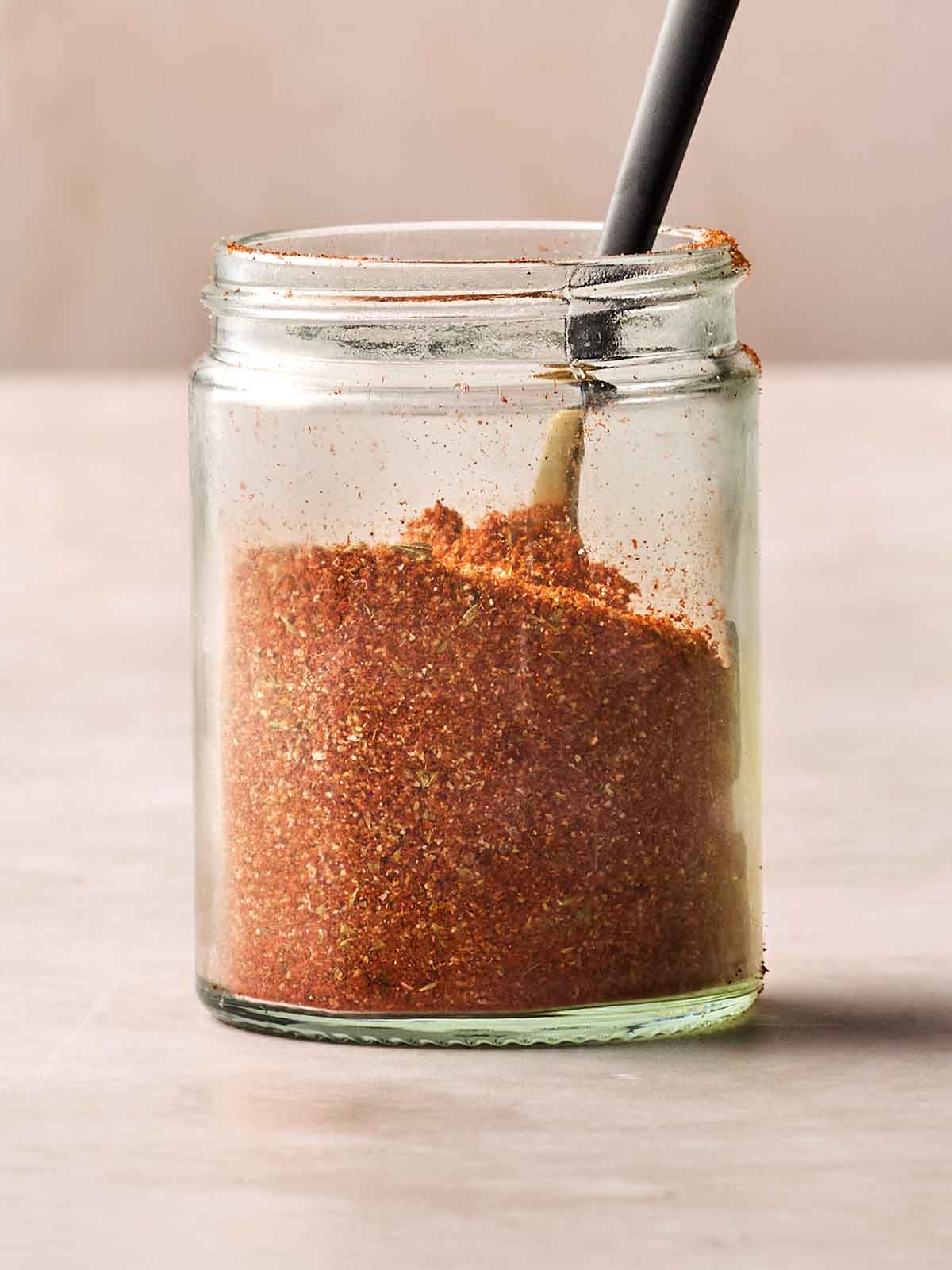 A small jar with homemade fajita mix inside, with a spoon in.