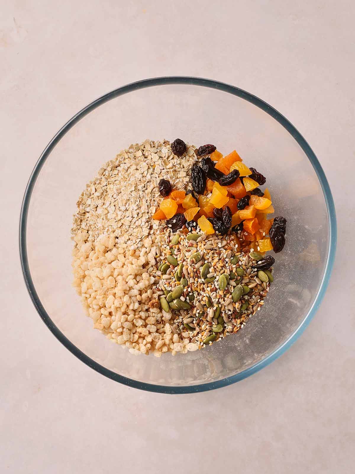 A glass bowl filled with oats, rice crispies, dried fruit and mixed seeds.