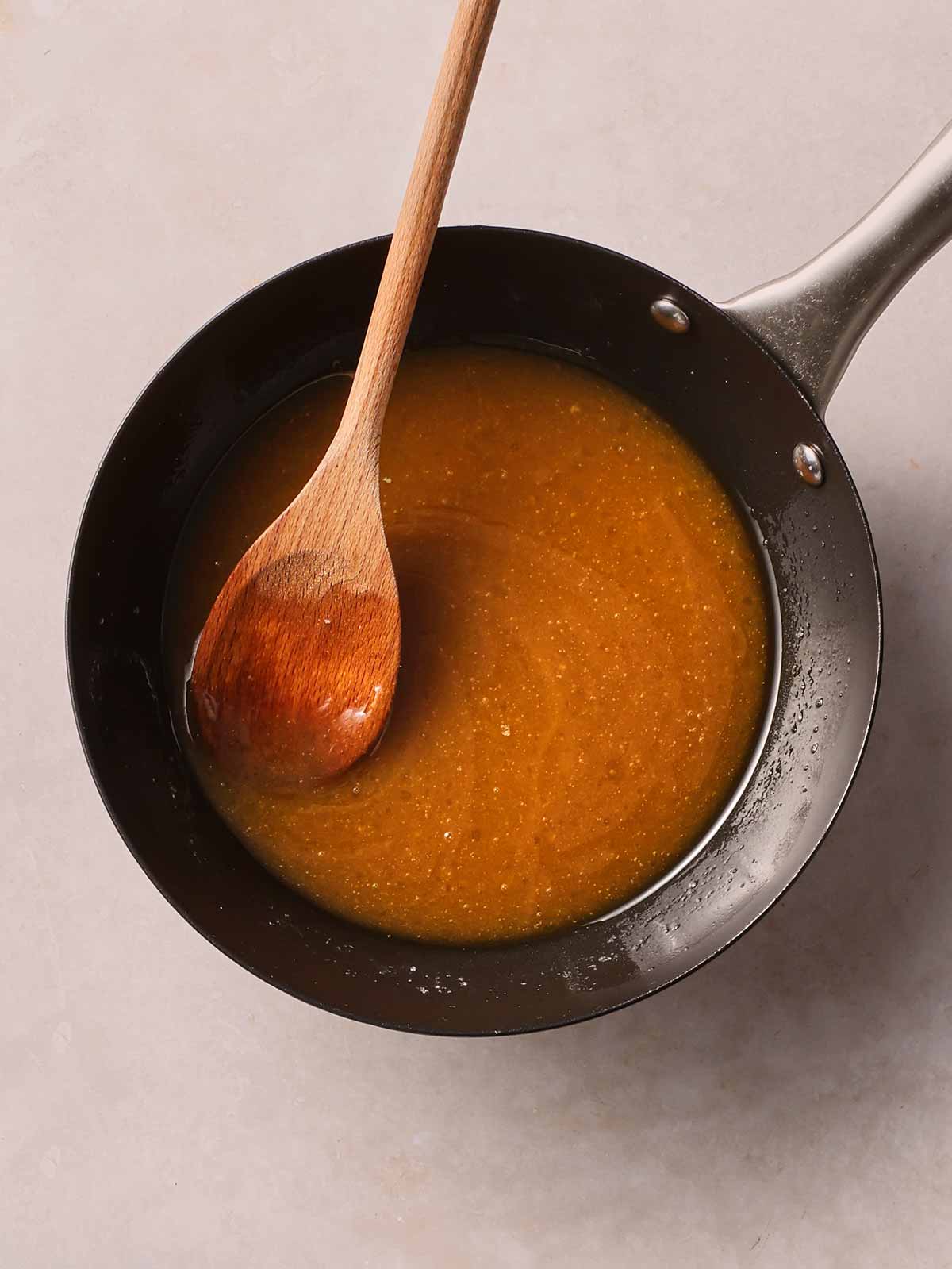 A pan with a brown mixture melted together, with a wooden spoon in.
