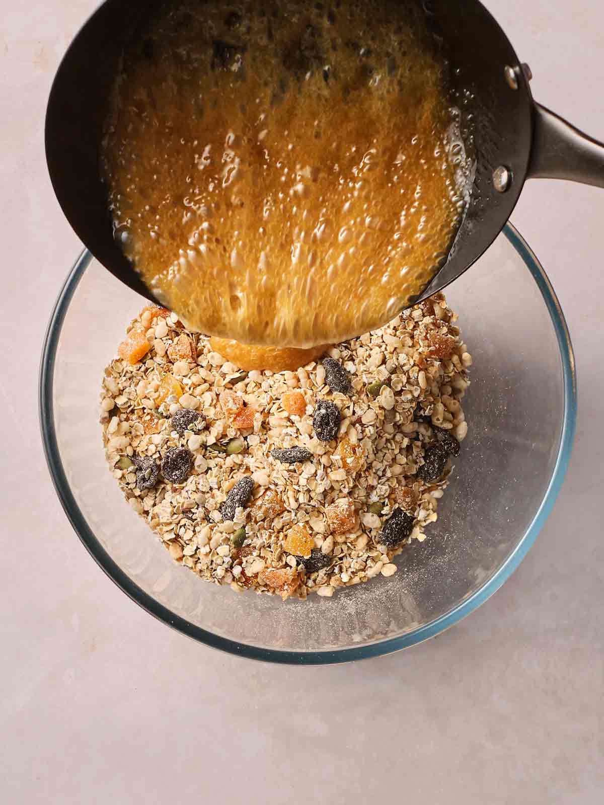 A glass bowl of mixed dry ingredients, with a pan above it pouring a brown, melted liquid into it.