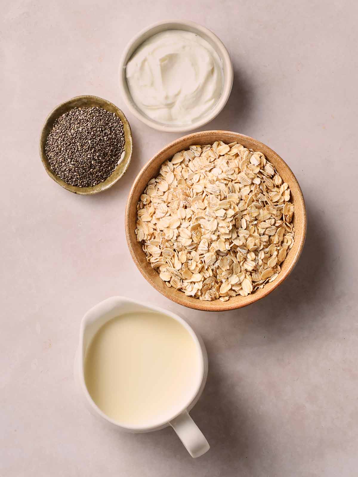 The basic ingredients for making Overnight Oats in bowls on a white counter top.