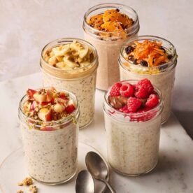 Five mason jars on a white counter, each with overnight oats in and each with different toppings.