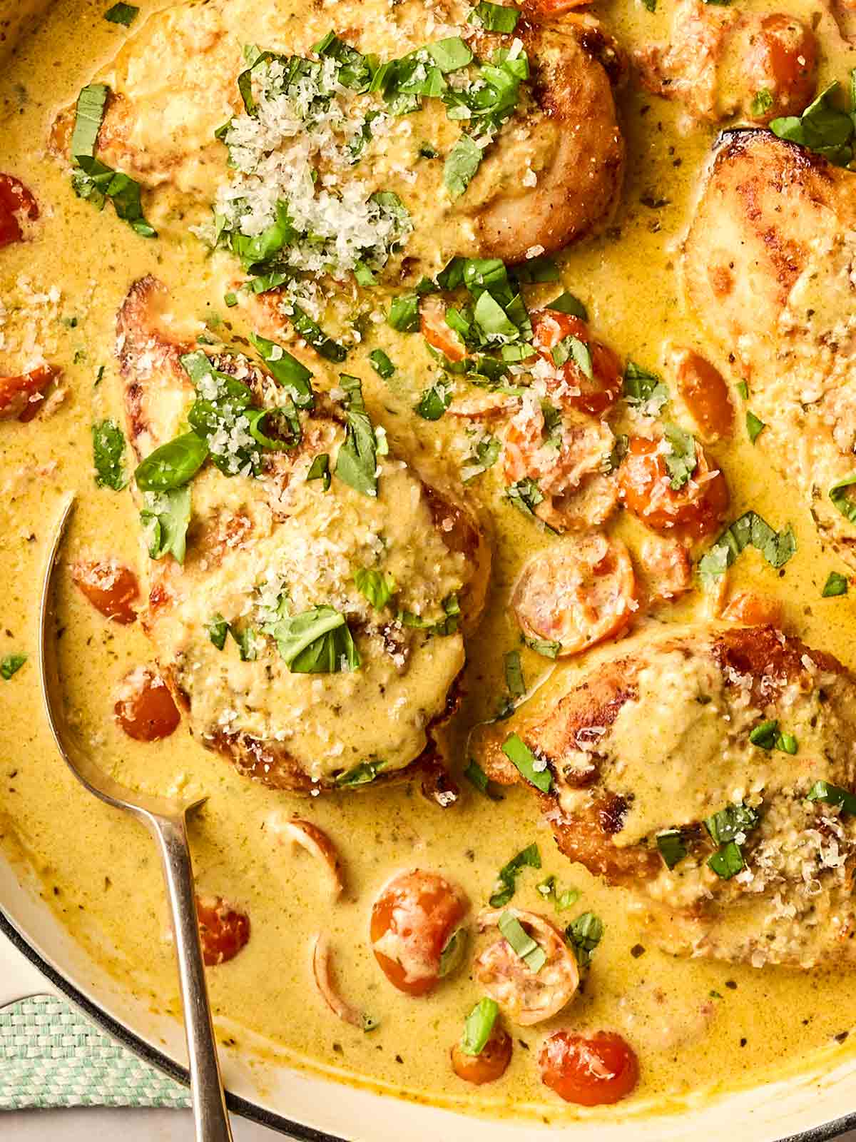 A pan of homemade pesto chicken in a creamy sauce, with a spoon, ready to serve.