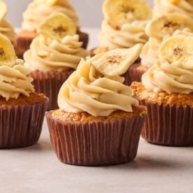 A side angle of banana cupcakes with buttercream on top and banana chips.