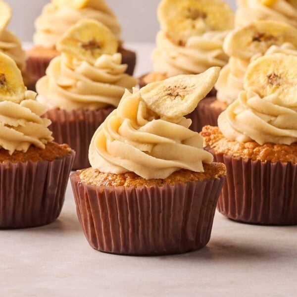 A side angle of banana cupcakes with buttercream on top and banana chips.