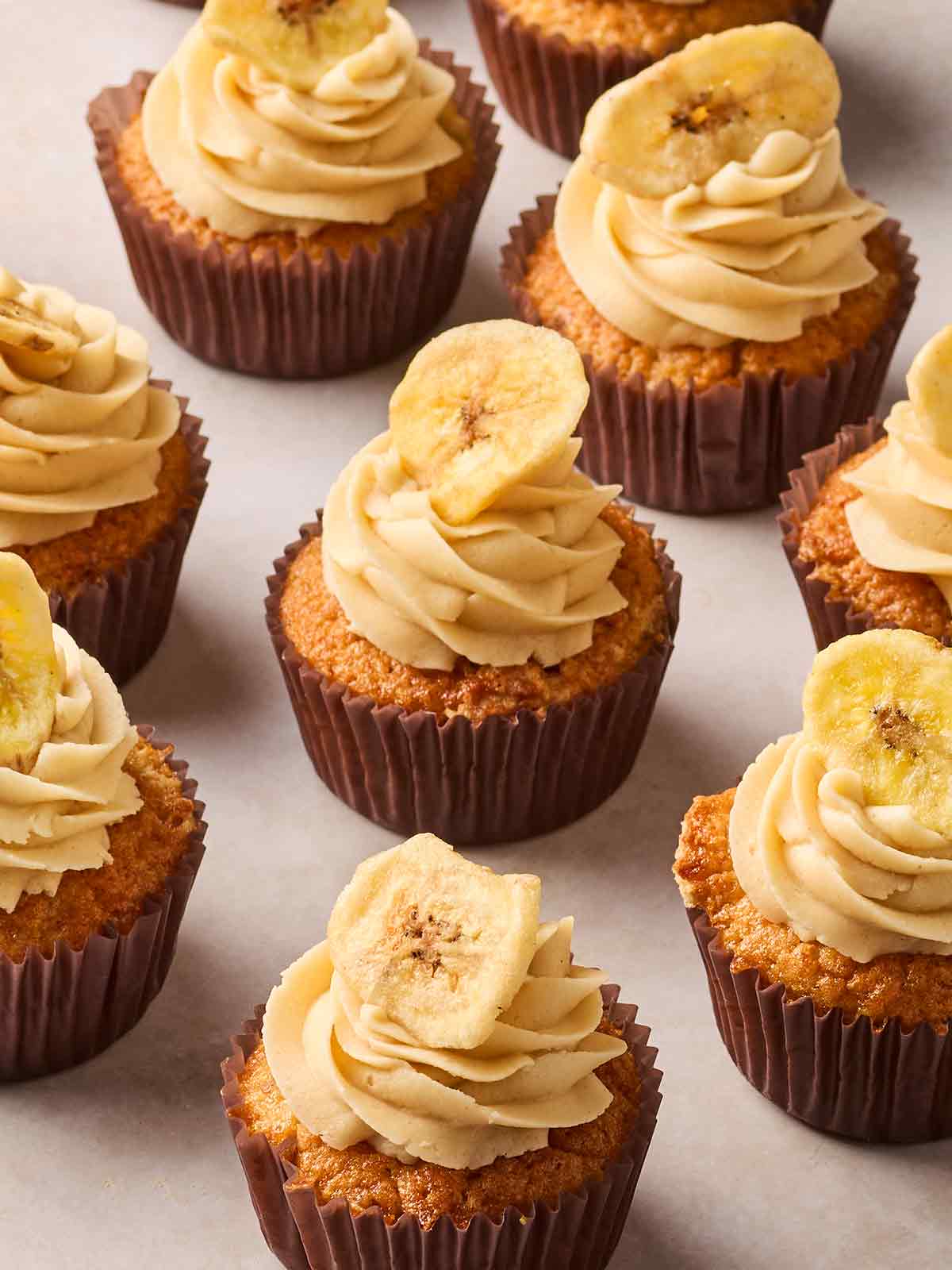 Looking down onto rows of banana cupcakes on a white clear surface.