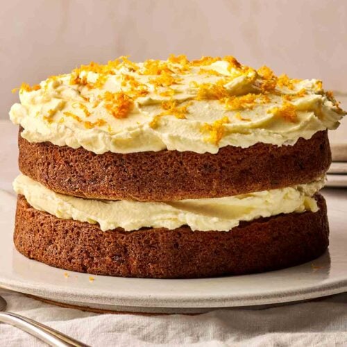 A side view of a simple homemade Carrot Cake, on a plate on a table, ready to slice.