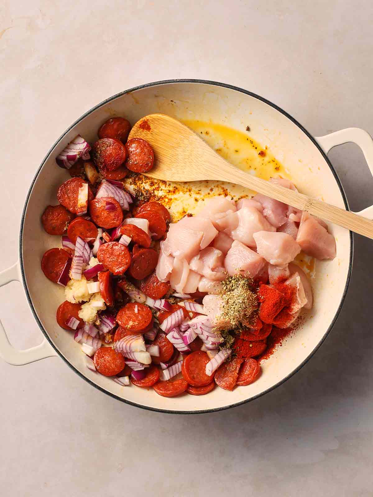 A pan with chorizo, red onion, raw cubed chicken and herbs starting to cook.