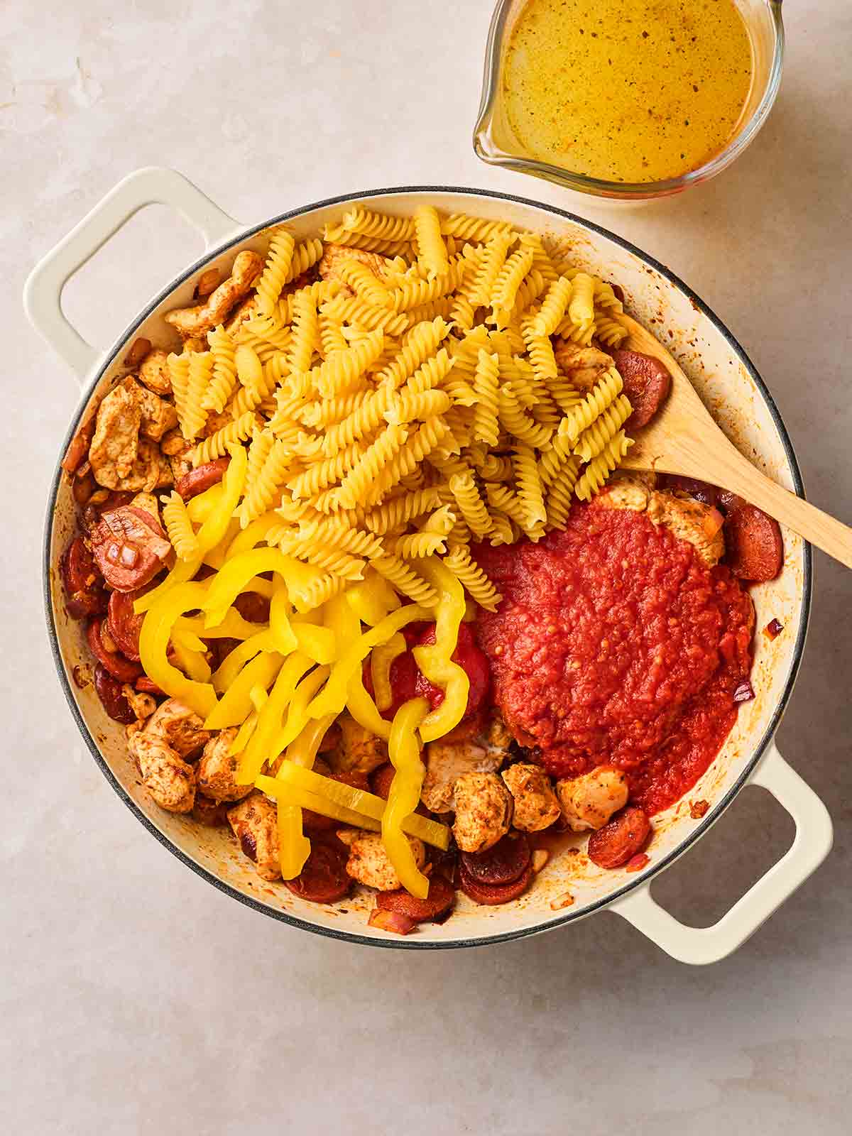 A pan with ingredient in on a white surface, including tinned tomatoes, chicken, sliced yellow pepper and uncooked pasta.