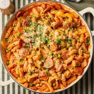 A close up of a pan of chicken and chorizo pasta in a tomato sauce with peas, on a table, ready to serve.