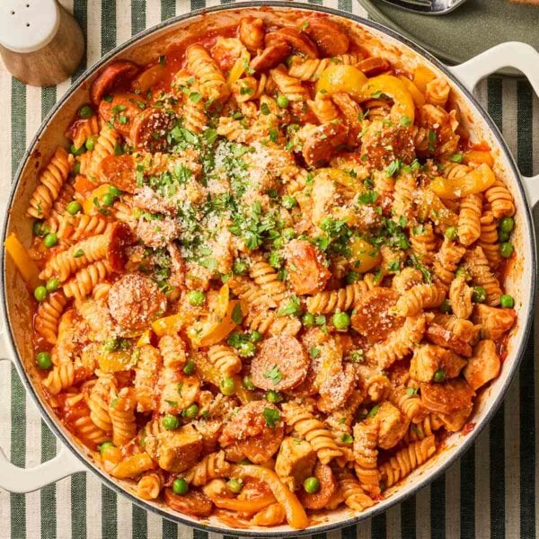 A close up of a pan of chicken and chorizo pasta in a tomato sauce with peas, on a table, ready to serve.