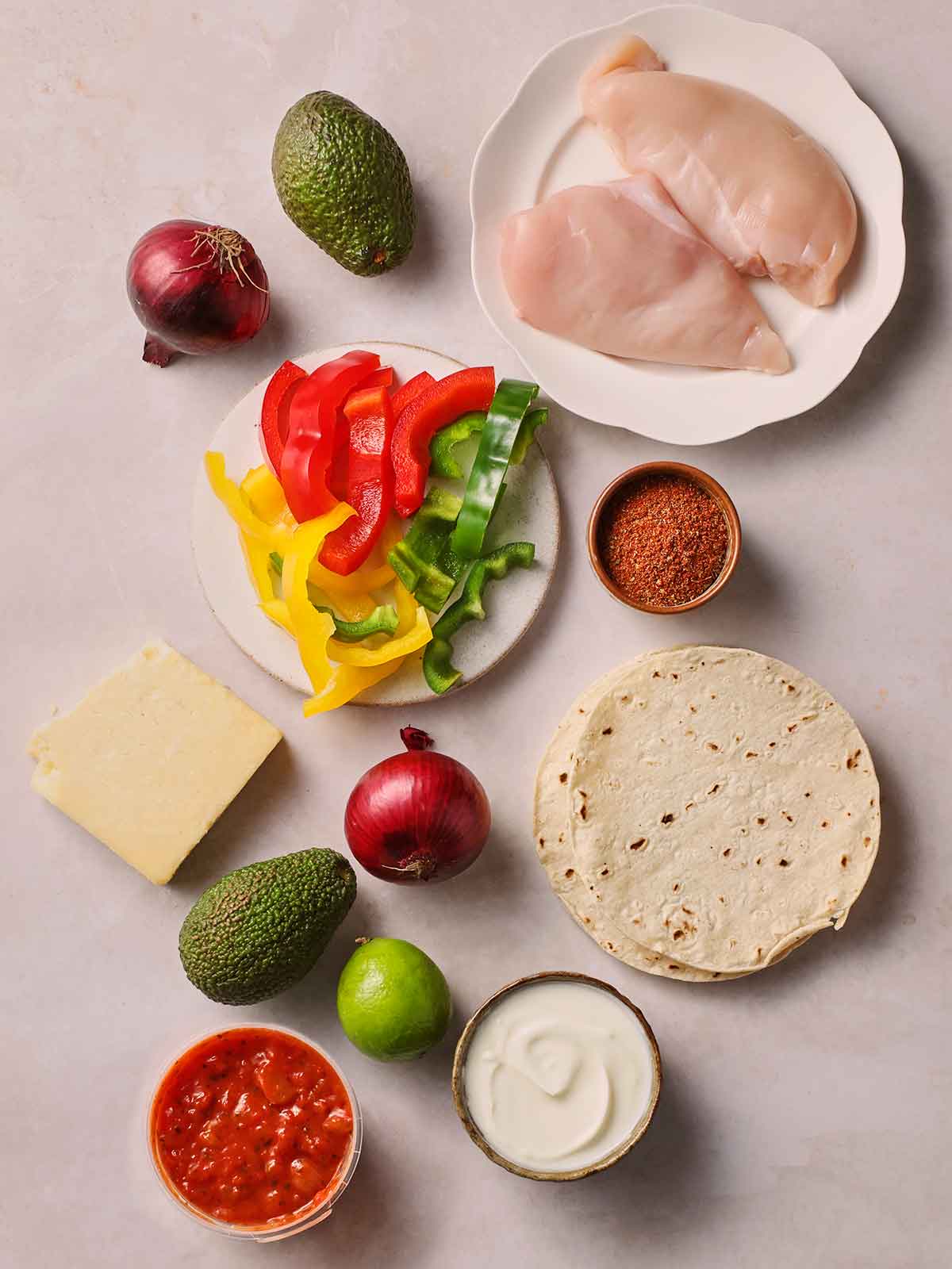 The raw ingredients for making chicken fajitas laid out on a white surface.