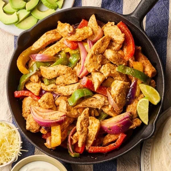 A pan filled with cooked chicken fajitas on a table, with side dishes around, ready to eat.